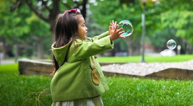 bambina al parco che gioca con le bolle di sapone